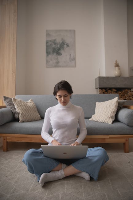 A relaxed woman working on a laptop at home while stretching her leg.